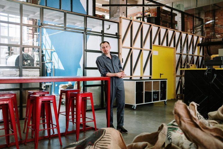 Man in a work uniform in an industrial loft setting with red furniture.